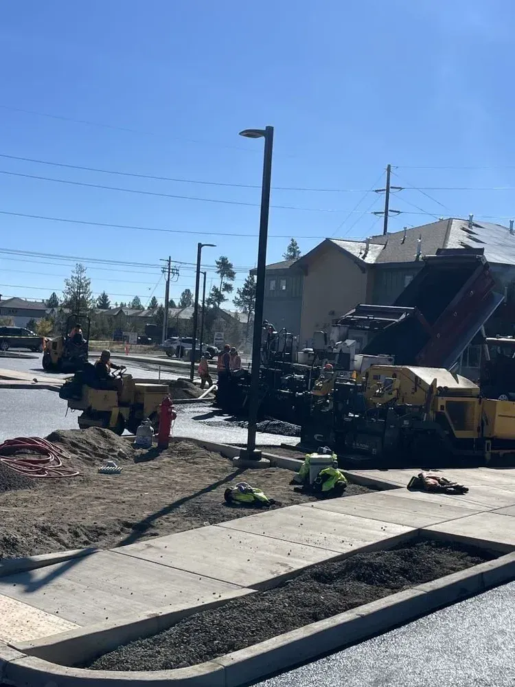 Construction work on a residential street with excavator, dirt piles, and a house in the background