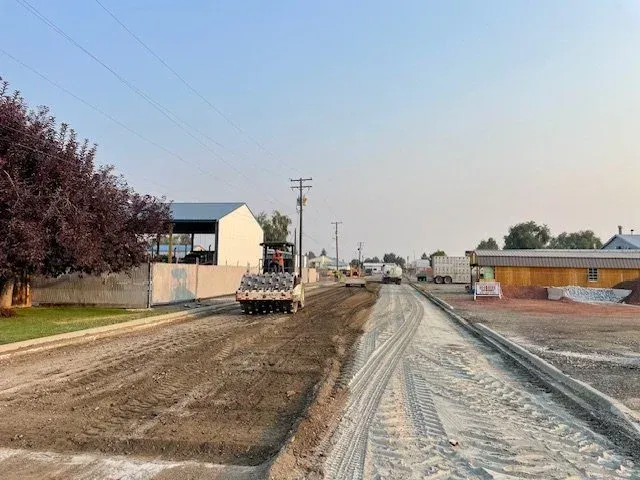 Road construction beside houses, with a truck spreading dirt on a muddy, unfinished street.