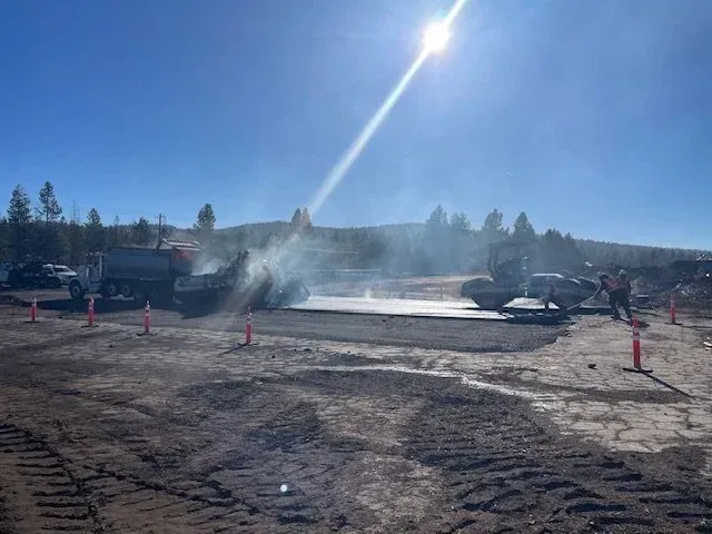 Cars on a smoky dirt lot with traffic cones under bright sun, as someone sprays water nearby
