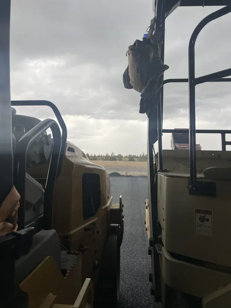 Two parked construction vehicles on a wet lot under a cloudy sky