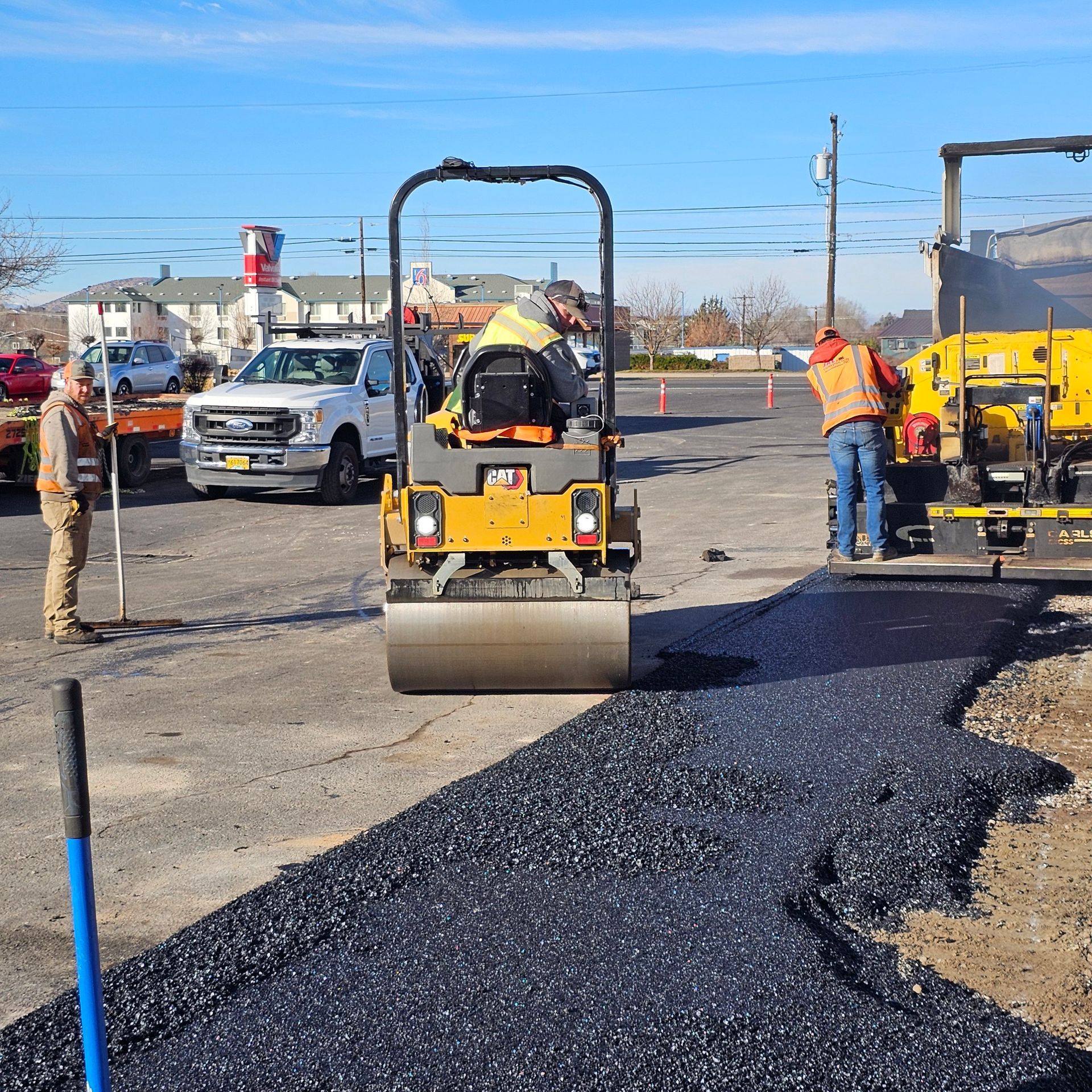 Road crew paving a street with a yellow roller and fresh black asphalt under a clear sky