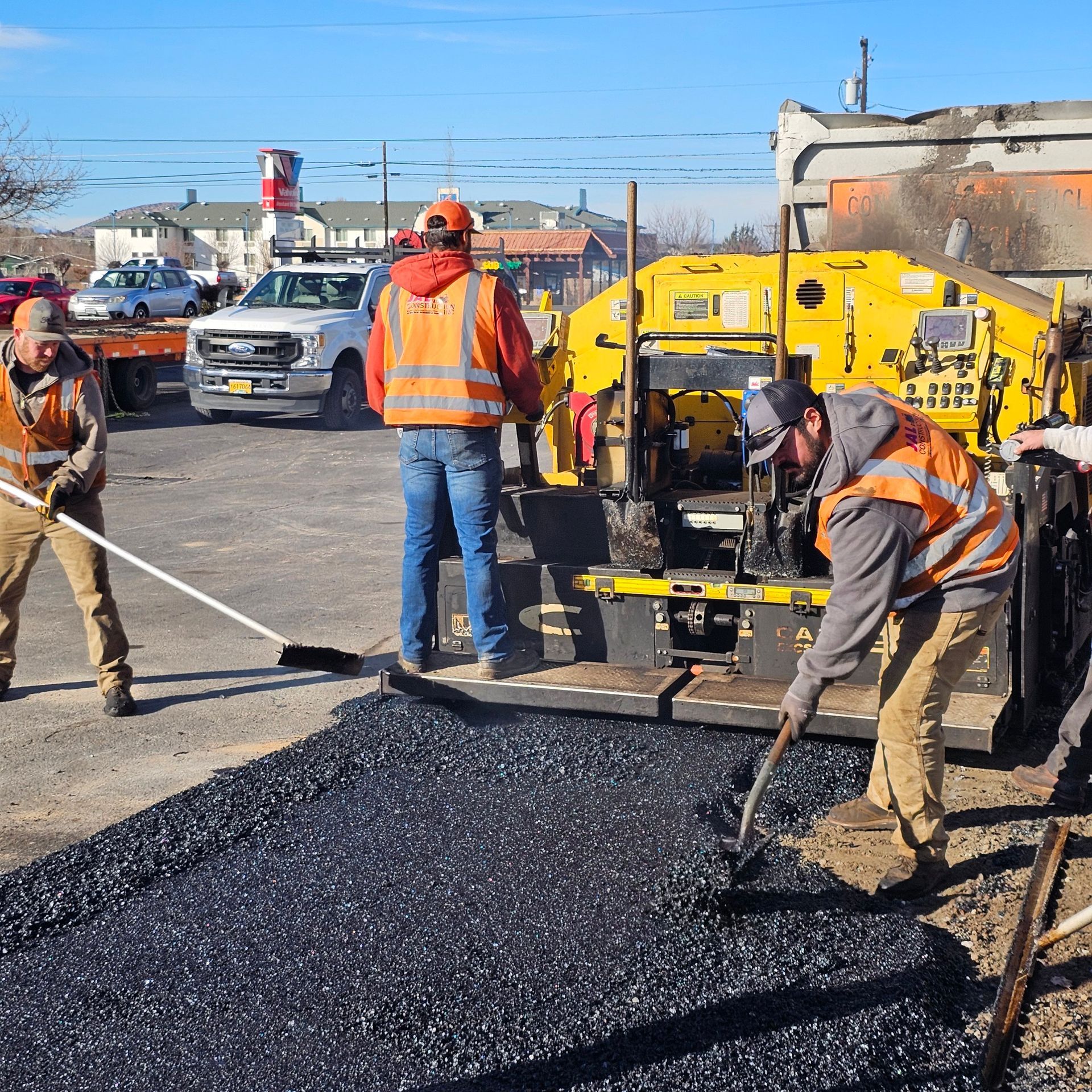 Road crew paving asphalt with machinery and orange safety vests on a city street