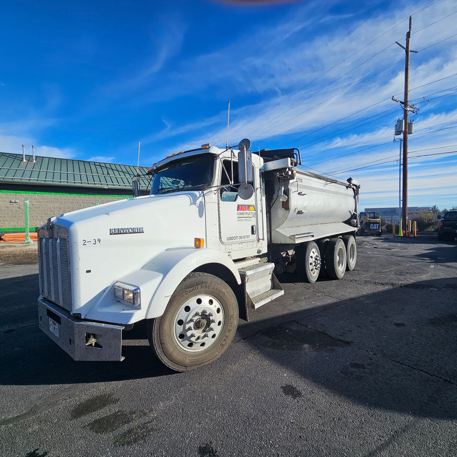 White dump truck parked on a gravel lot under a blue sky with streaked clouds