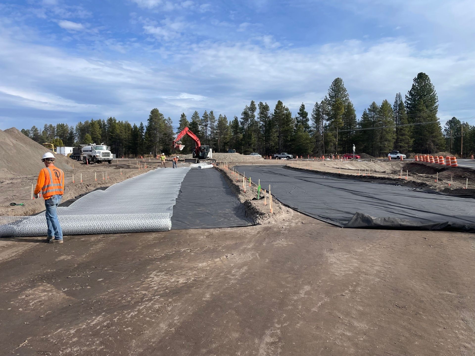Construction site with worker, excavator, and gravel roadbed under clear sky
