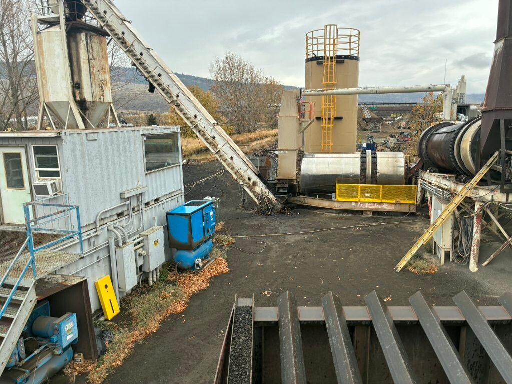 Industrial plant with conveyor belts, blue equipment, and large metal tanks in an outdoor gravel yard