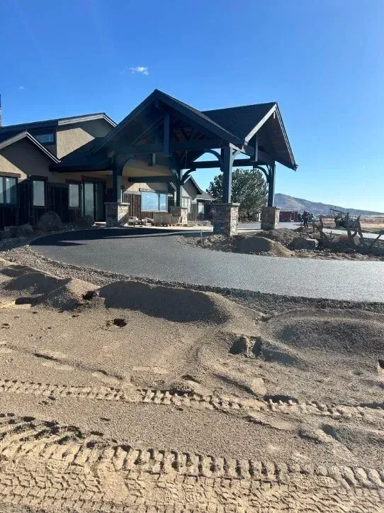 Sandy beach beside a modern lodge with a covered deck and distant water under a clear sky