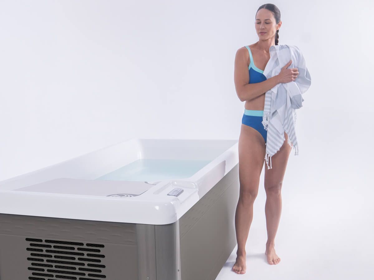 A woman in a bikini is standing next to a hot tub holding a towel.