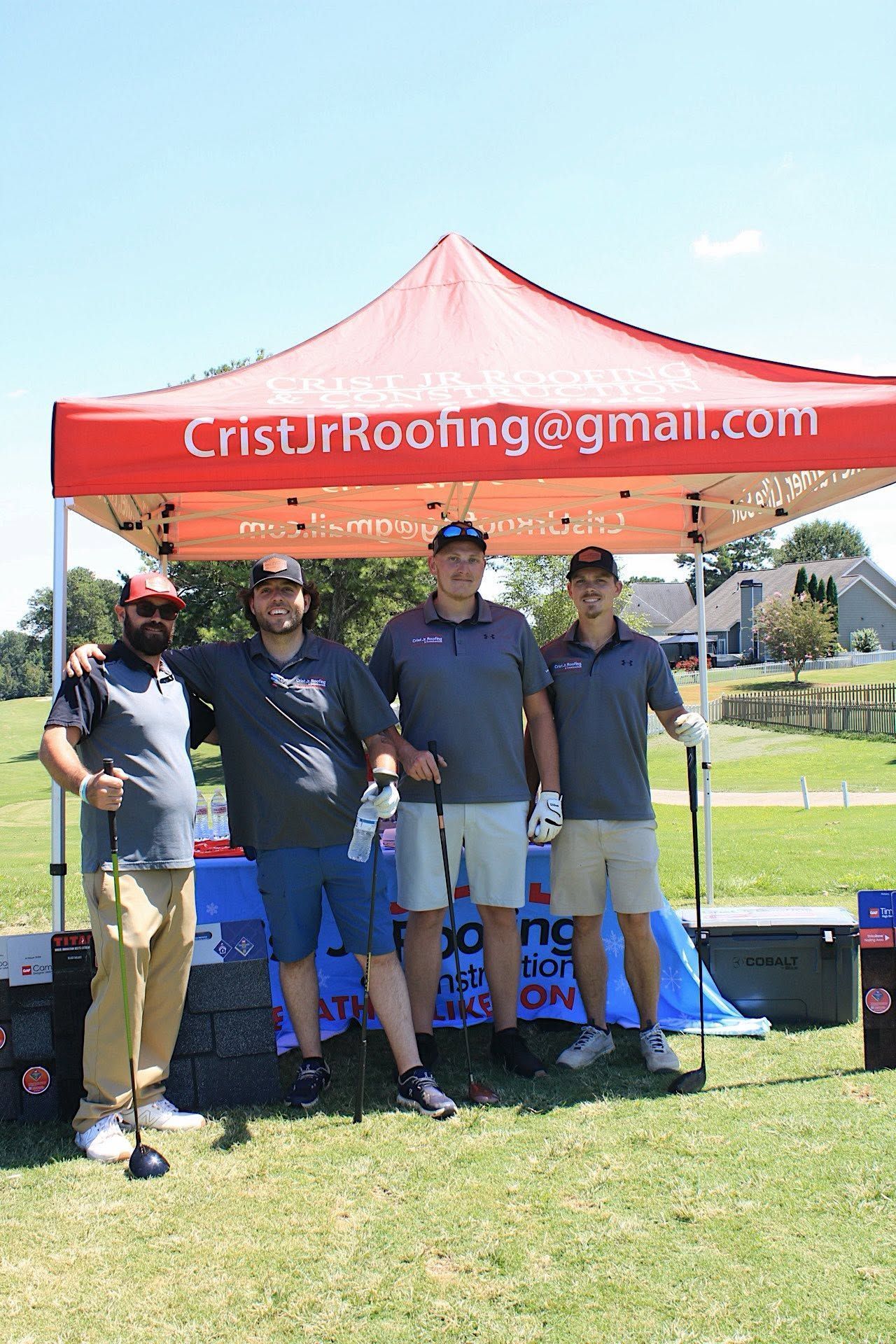 Five people posing under a red Crist Roofing canopy at an outdoor event.