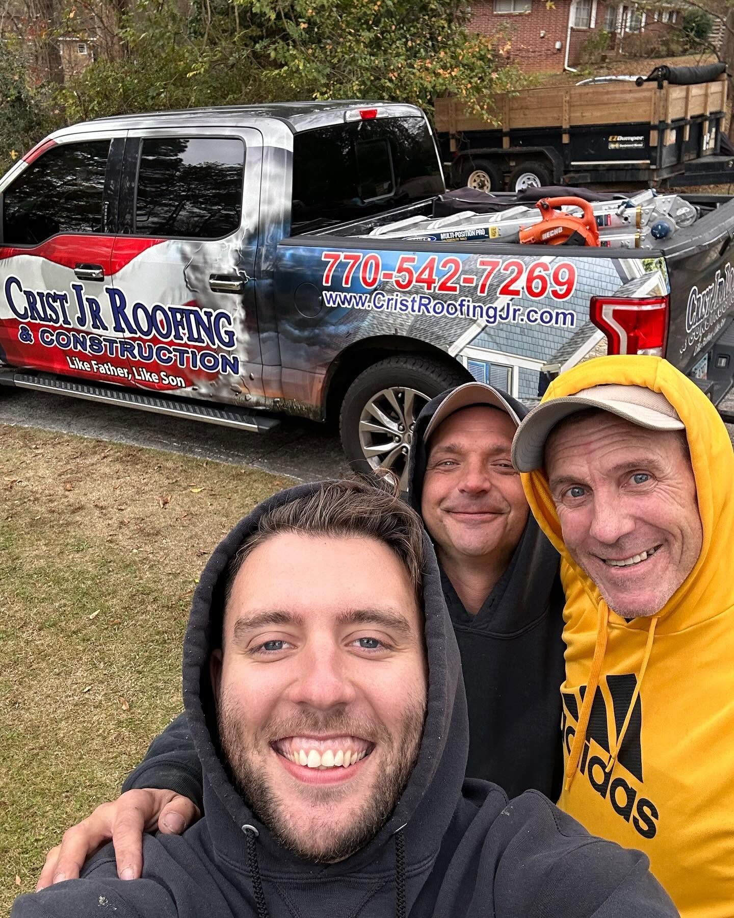 Three smiling people posing in front of a branded roofing pickup truck outdoors