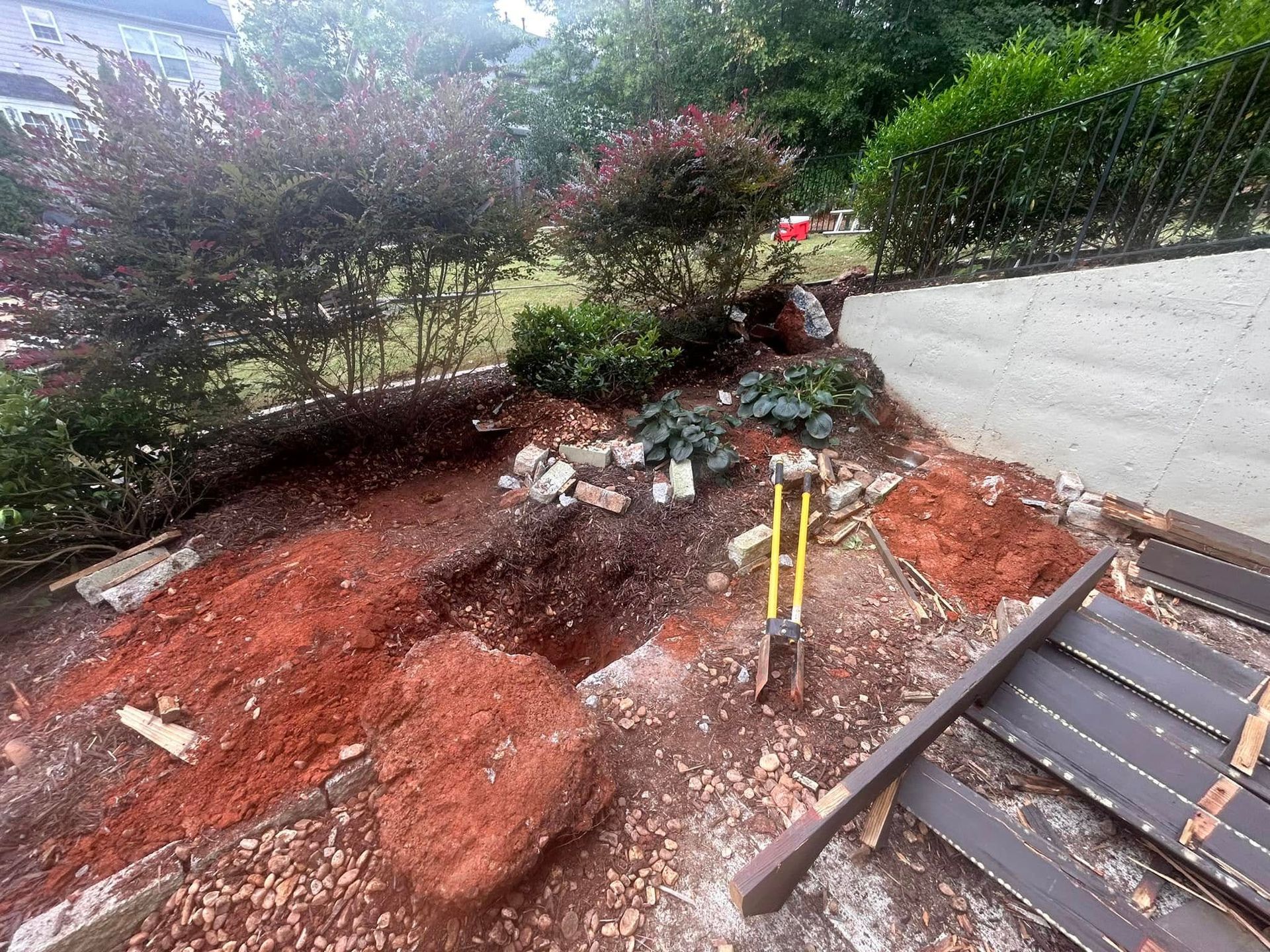 Rocky landscaped slope with red soil, shrubs, and a paved path beside a metal handrail under construction