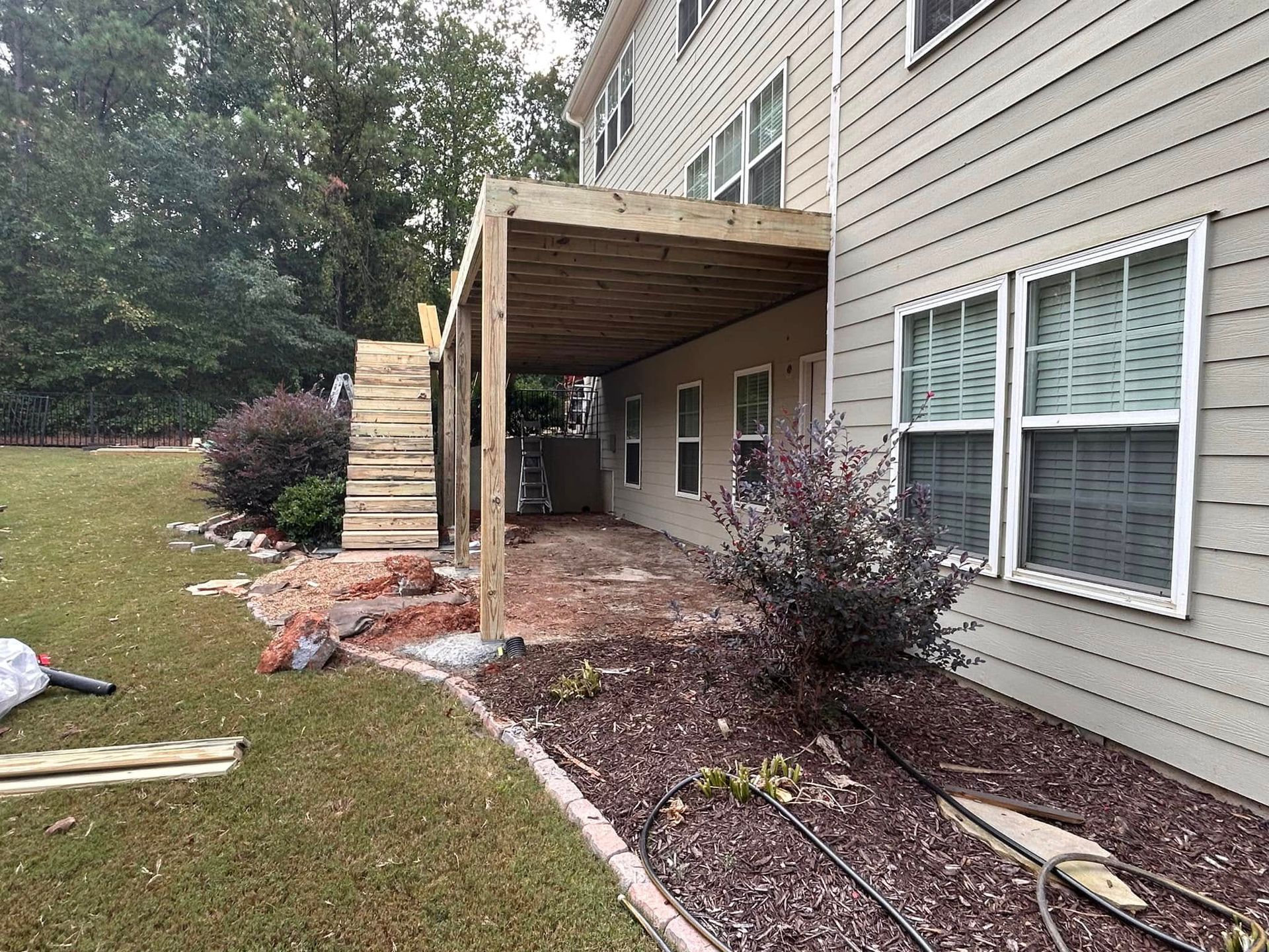 Backyard house exterior with a wooden covered patio and fresh landscaping beside beige siding
