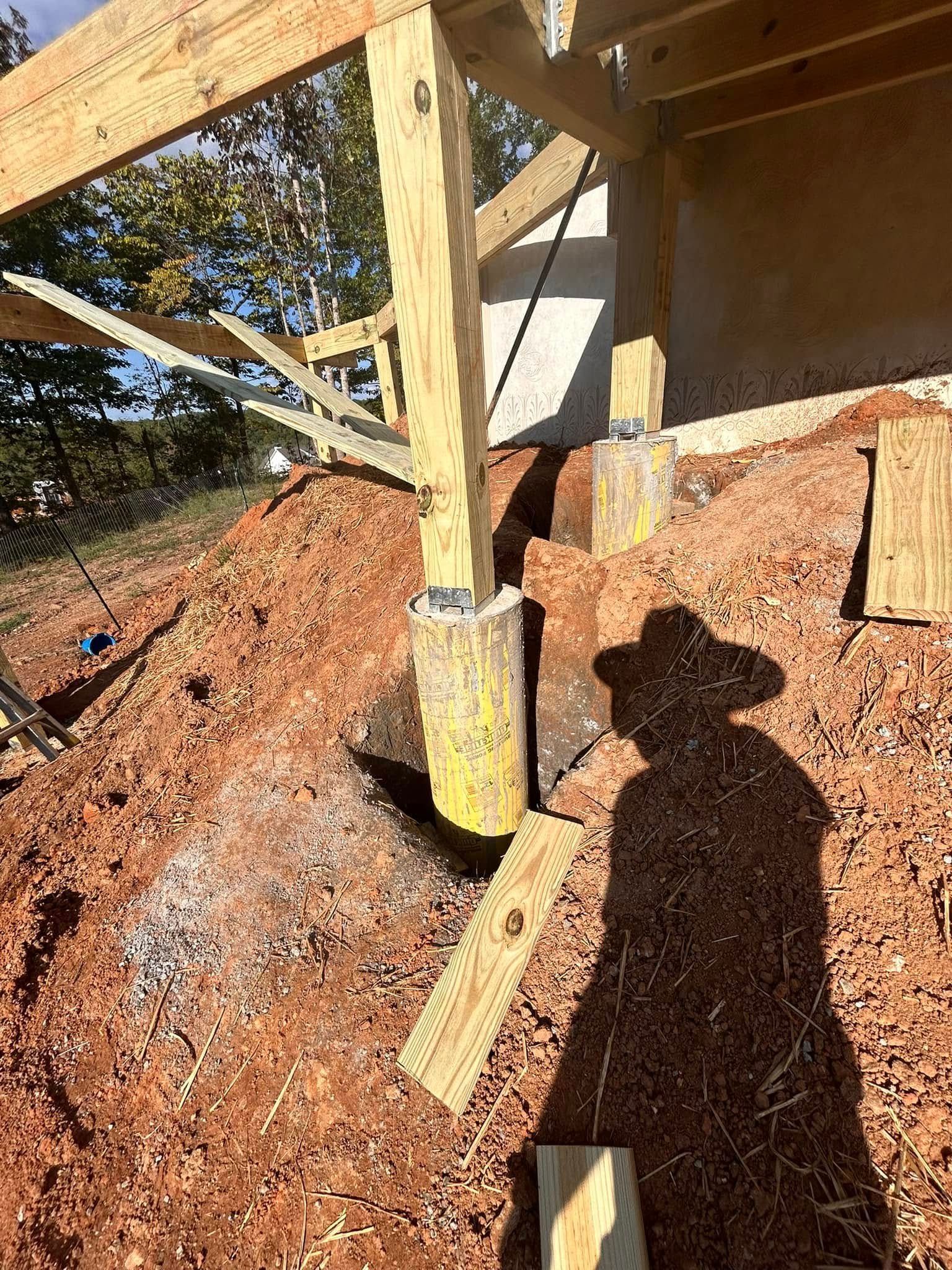 Construction site with wooden framing, a support post, and a dirt slope in bright sunlight.