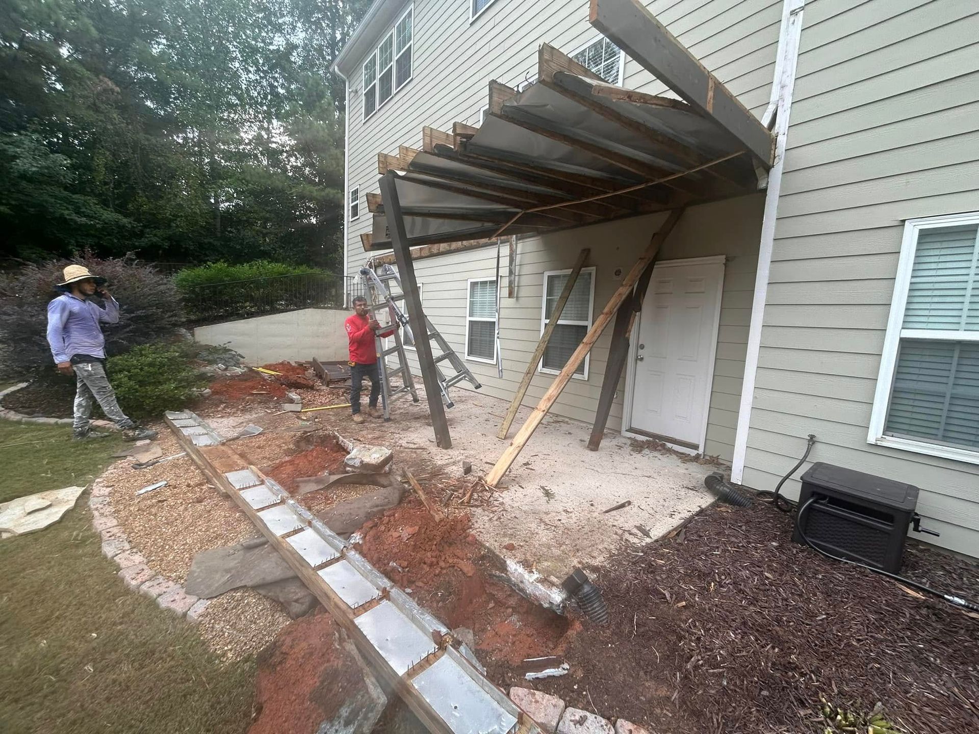 Workers brace a damaged townhouse overhang with wooden supports amid debris and dirt.