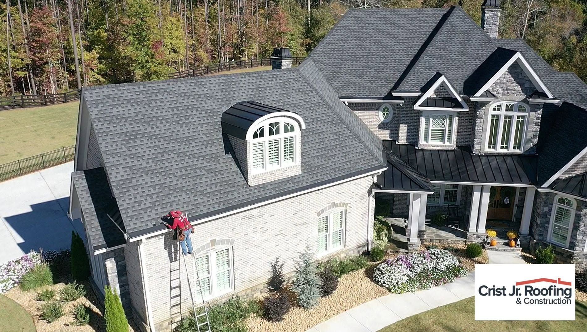 Aerial view of a gray house with a dormer roof and a black house beside it, with a person on the front wall