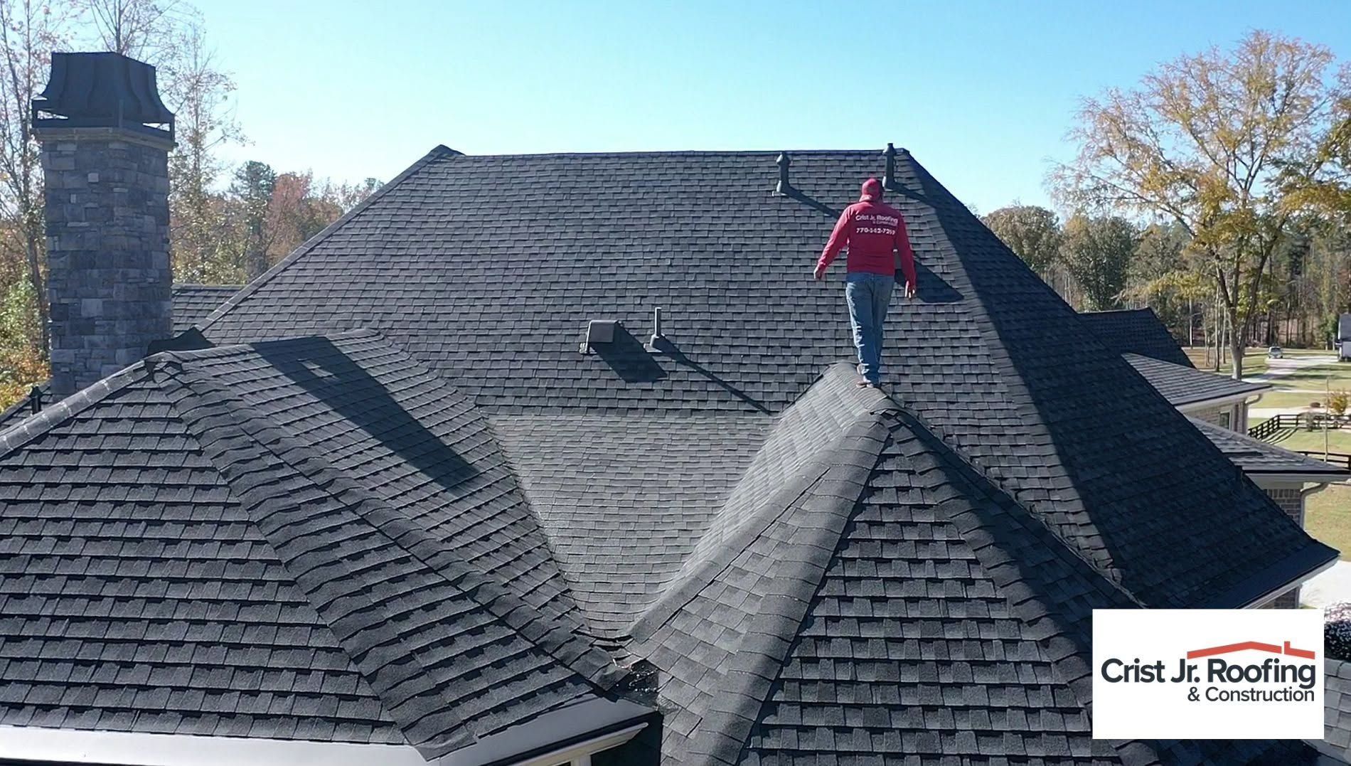 Worker on a gray shingled roof with a chimney in a residential neighborhood.