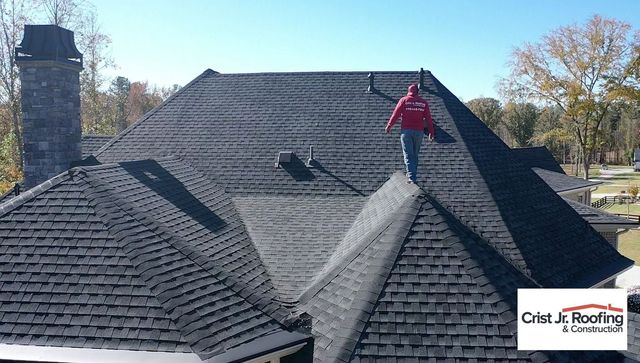 Worker on a dark shingled roof inspecting a ridge vent on a suburban home
