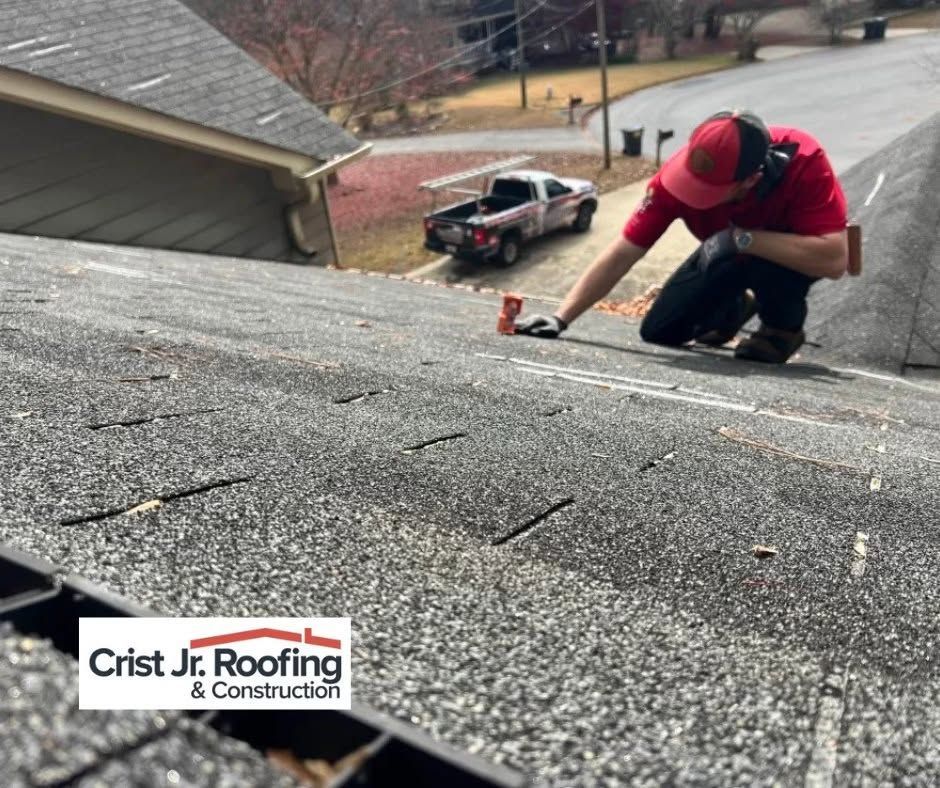 Roofing worker in red shirt repairing a gray shingle roof with a tool.