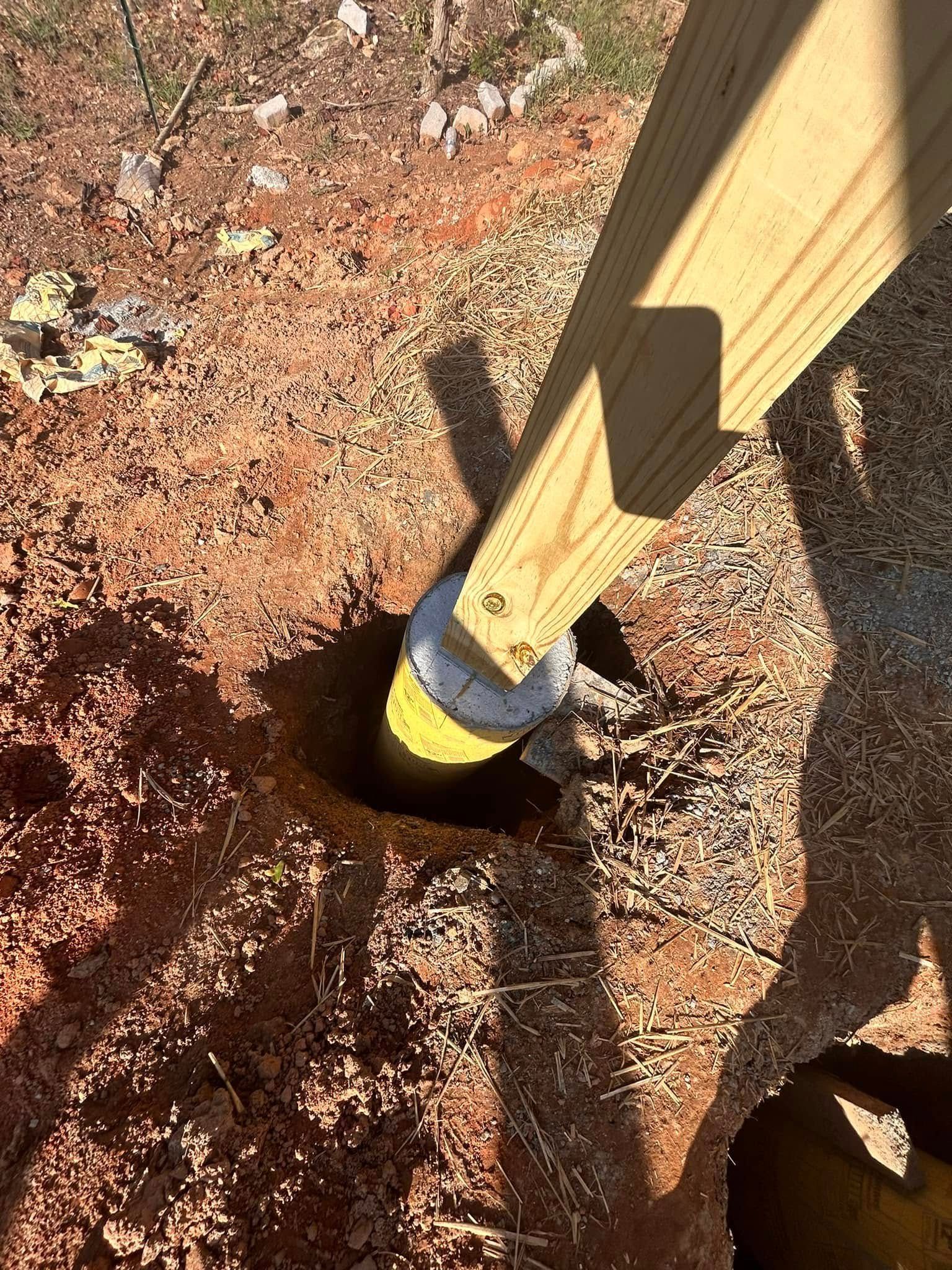 Wooden fence post set in freshly dug soil with a yellow protective sleeve at the base