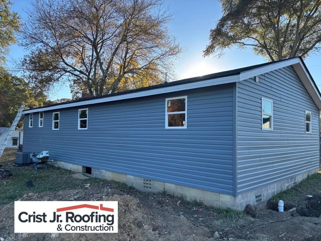 Blue house exterior with new gray roof and Crist Jr. Roofing logo