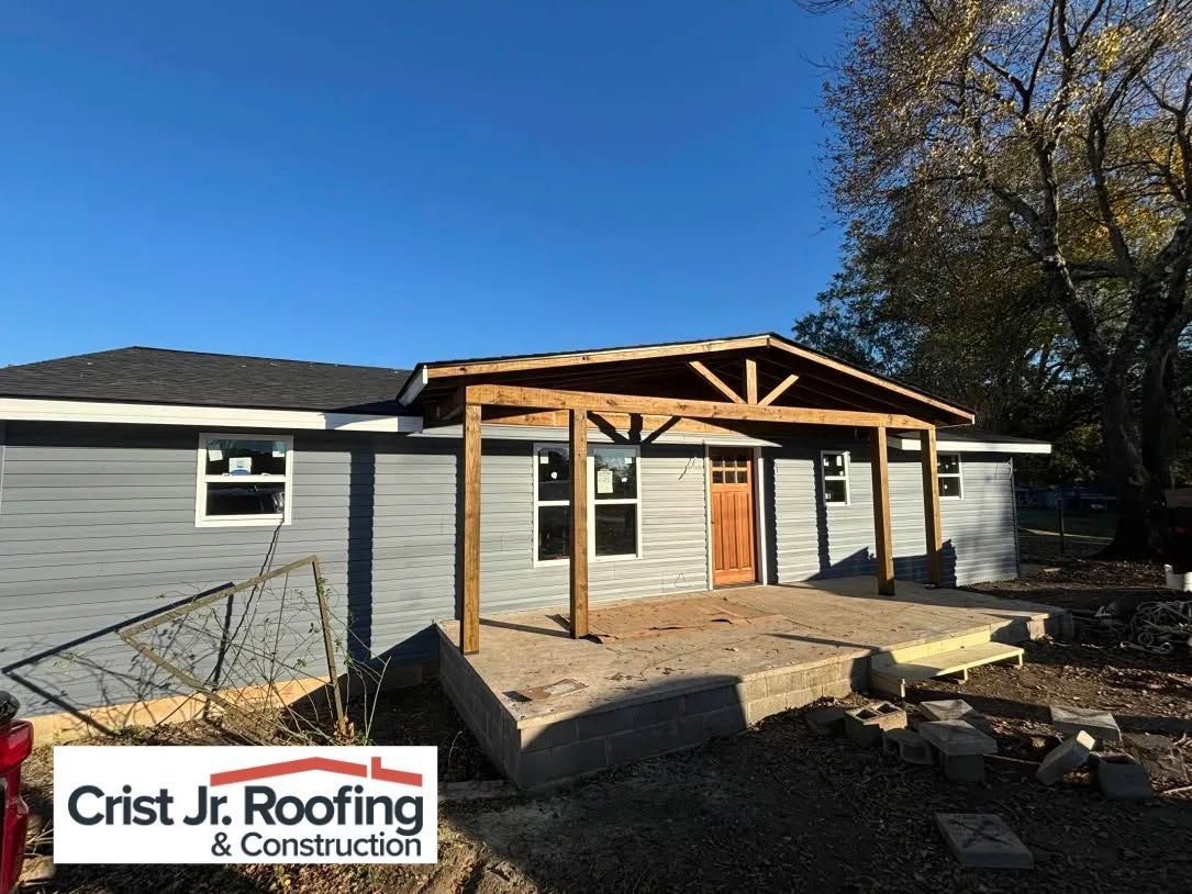 House exterior with gray siding and a new wooden porch under construction, Crist Jr. Roofing logo visible