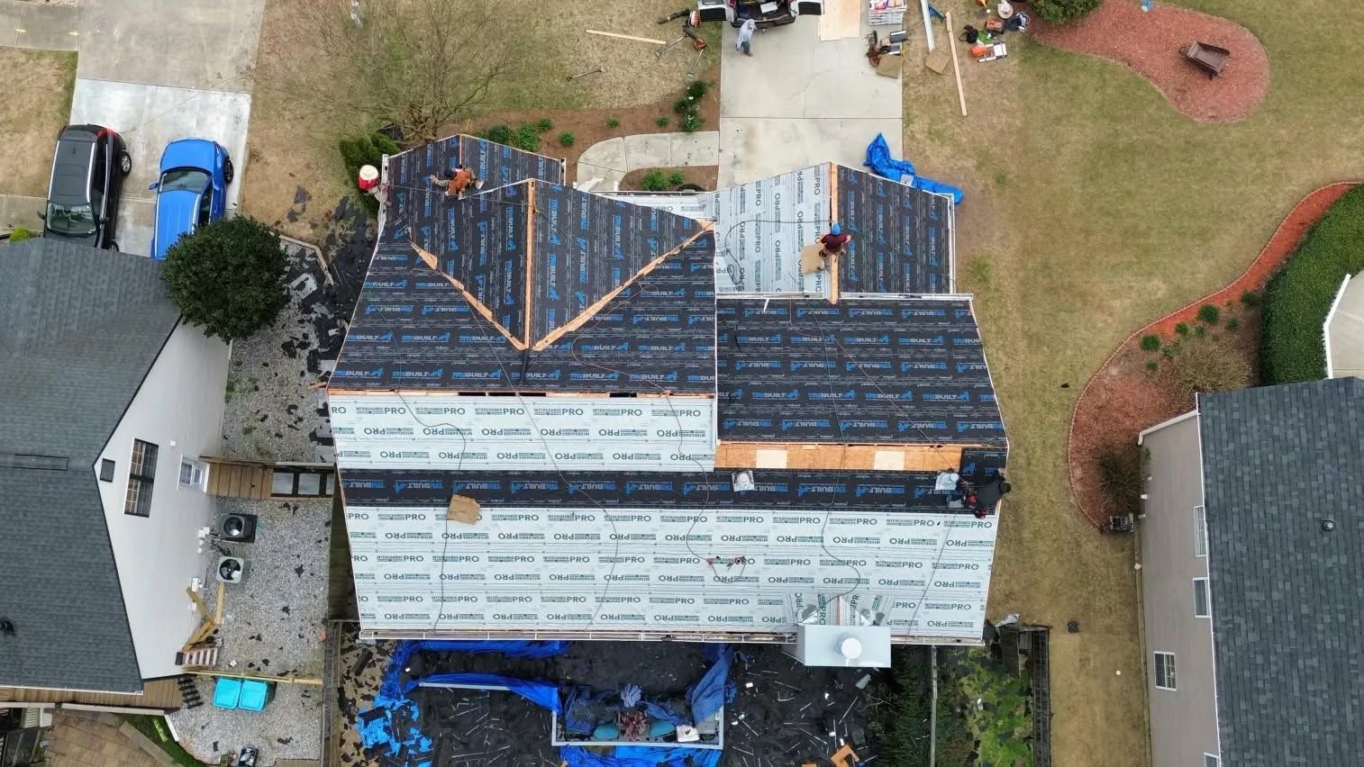Aerial view of a house with a partially replaced dark roof and construction materials in the yard