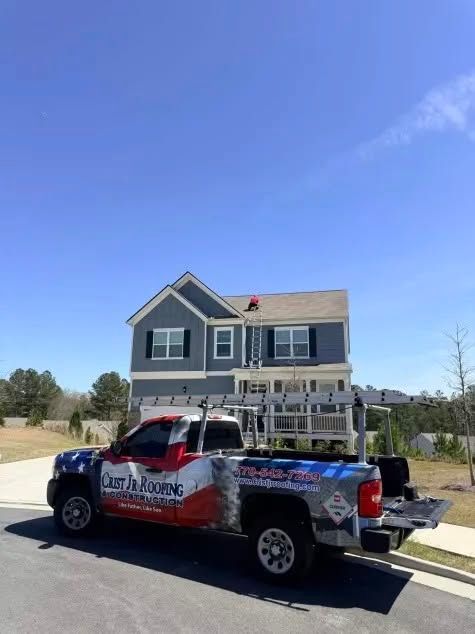 Blue-and-red utility truck parked in front of a gray two-story house under a clear sky.
