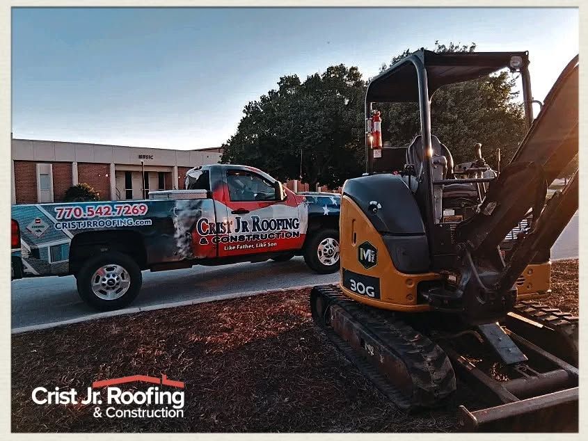 Crist J.R. Roofing pickup beside a yellow excavator at a construction site at sunset