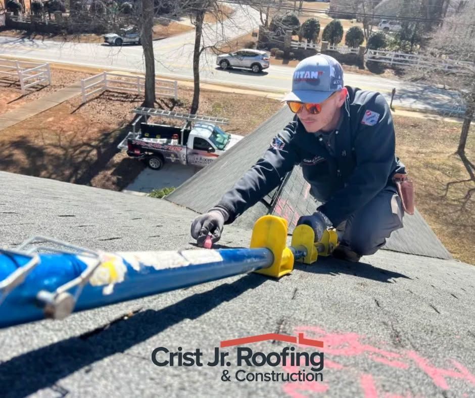 Roofing worker securing blue tarp on a steep roof with yellow tool, wearing blue cap and gloves