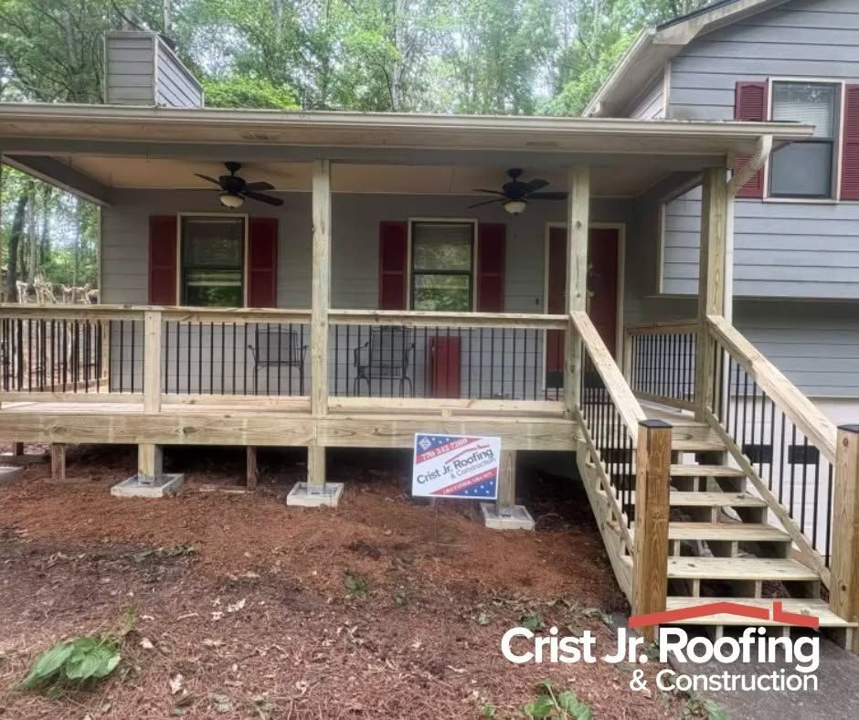 Front porch of a gray house with red shutters, stairs, and a Crist Jr. Roofing sign below the deck