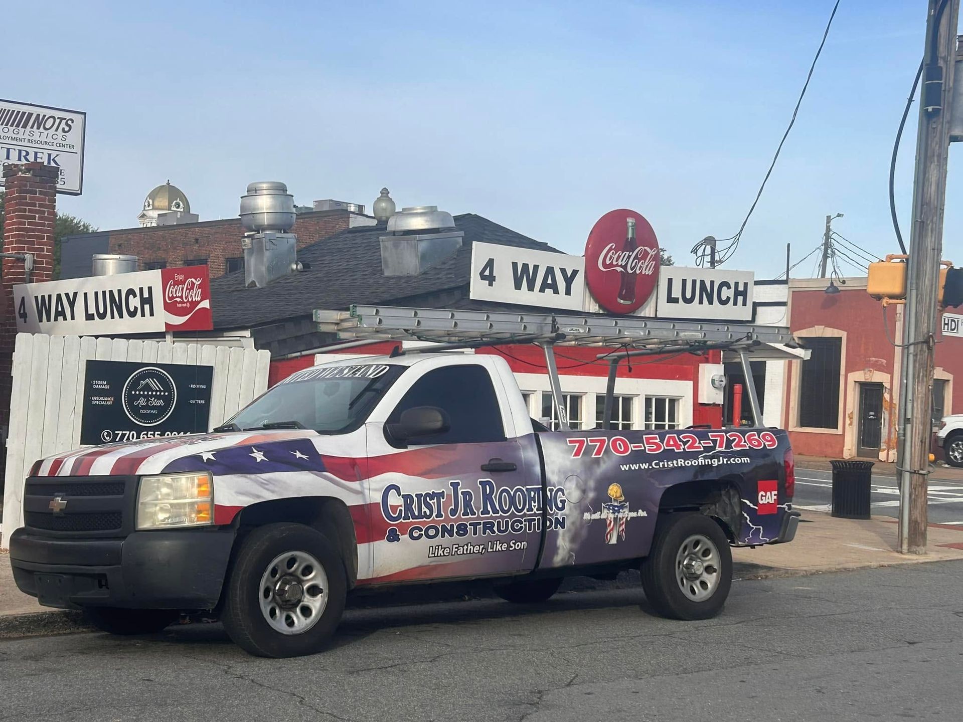 Tow truck parked outside 4 Way Lunch diner, with red-white-blue graphics and a Coca-Cola sign