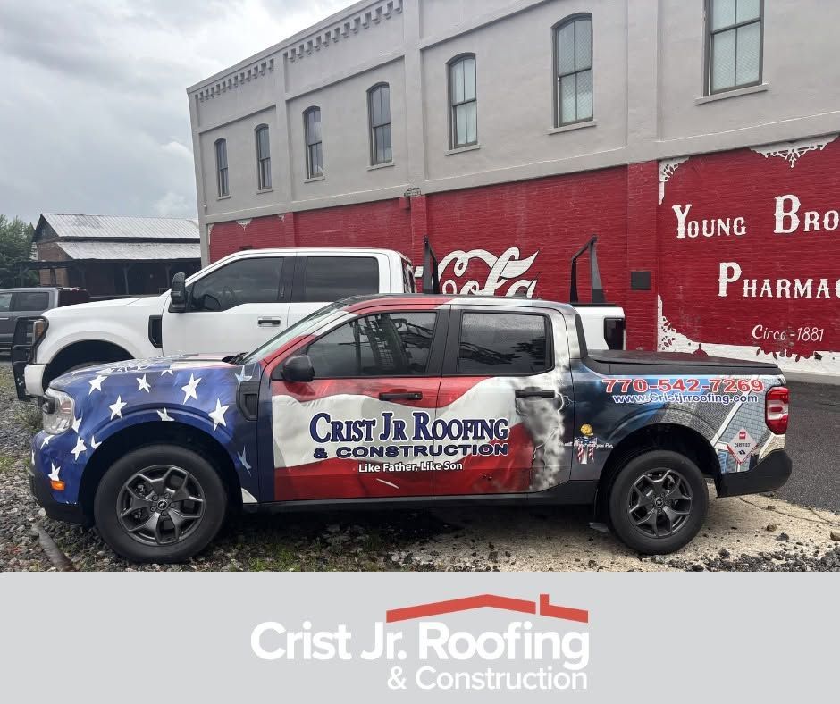 Wrapped pickup truck with stars and logo parked on gravel beside a brick building, Crist Jr Roofing & Construction