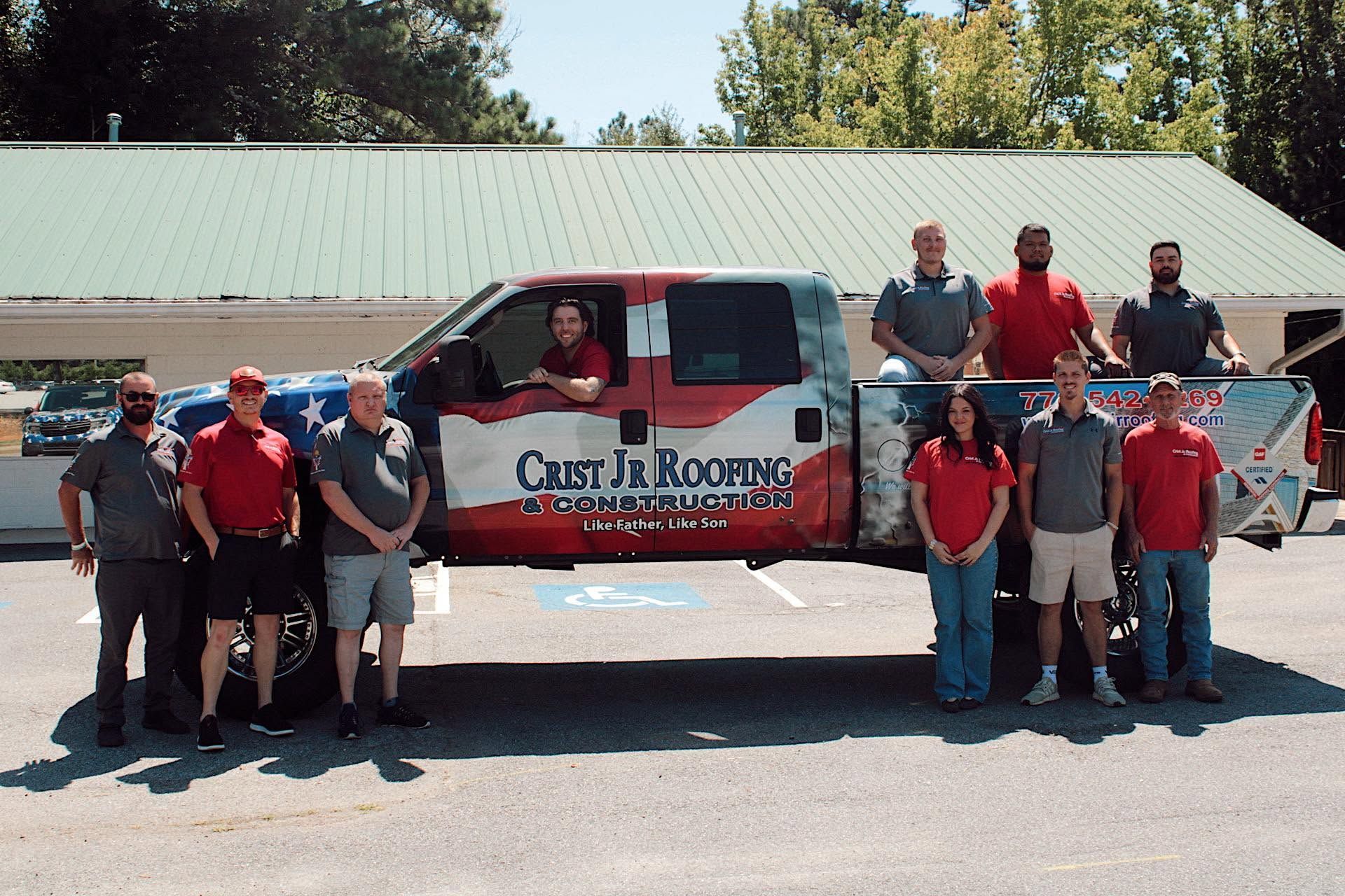 Group posing in front of a red roofing company truck in a parking lot