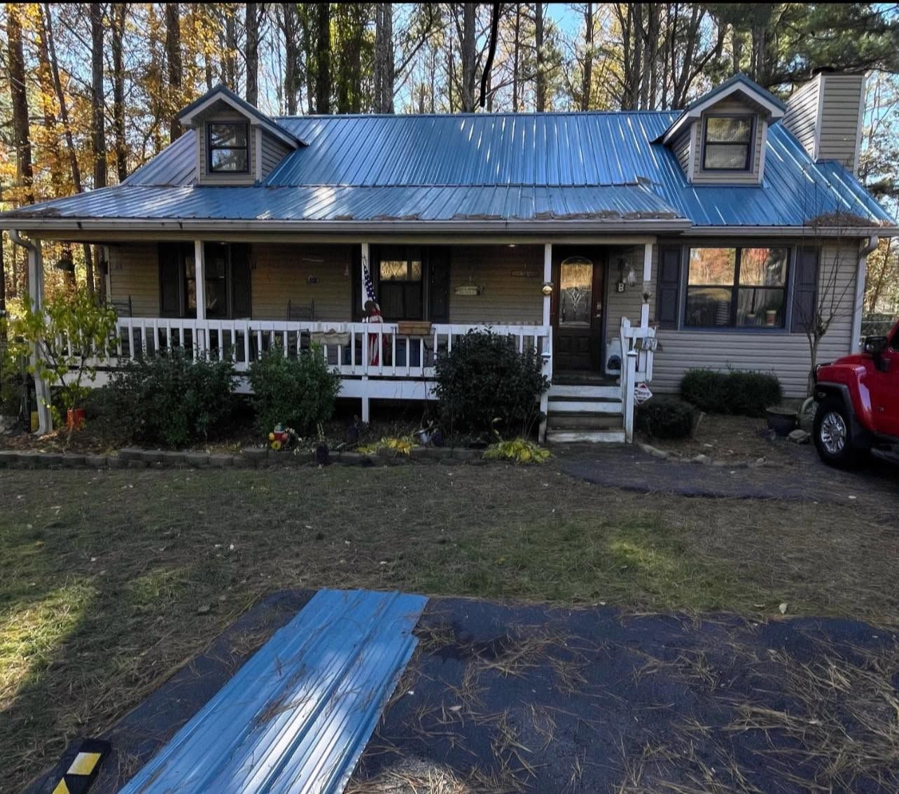 Wooden house with front porch and ramp, surrounded by trees, with a red truck parked beside it.