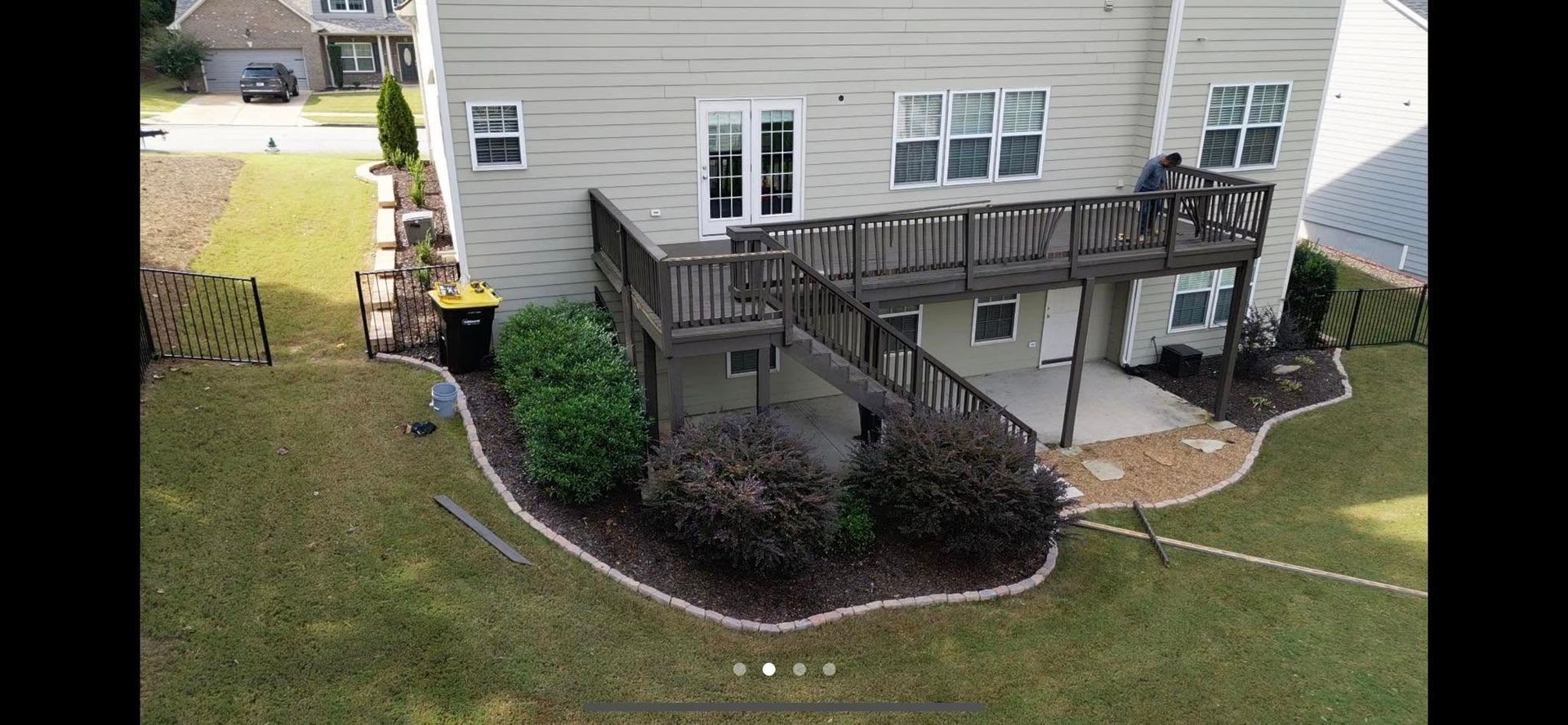 Backyard deck and stairs attached to a beige house, with landscaped shrubs and lawn.