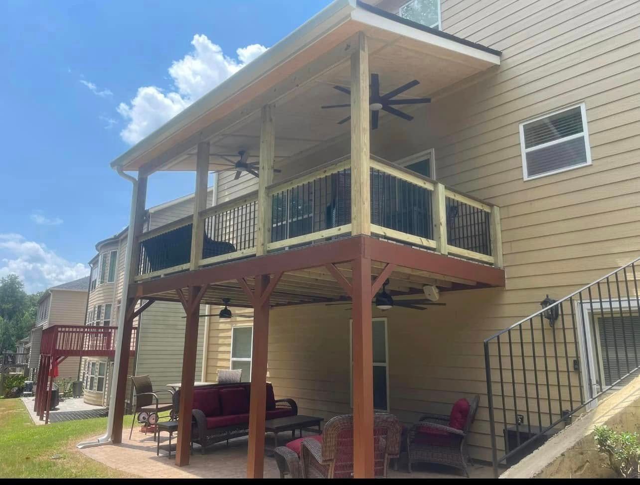 Two-story tan house with an elevated porch, red posts, ceiling fan, and patio furniture underneath.