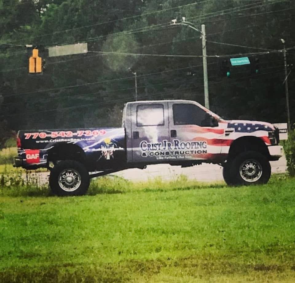 White utility pickup truck with company lettering parked on grass by a road, near a traffic light