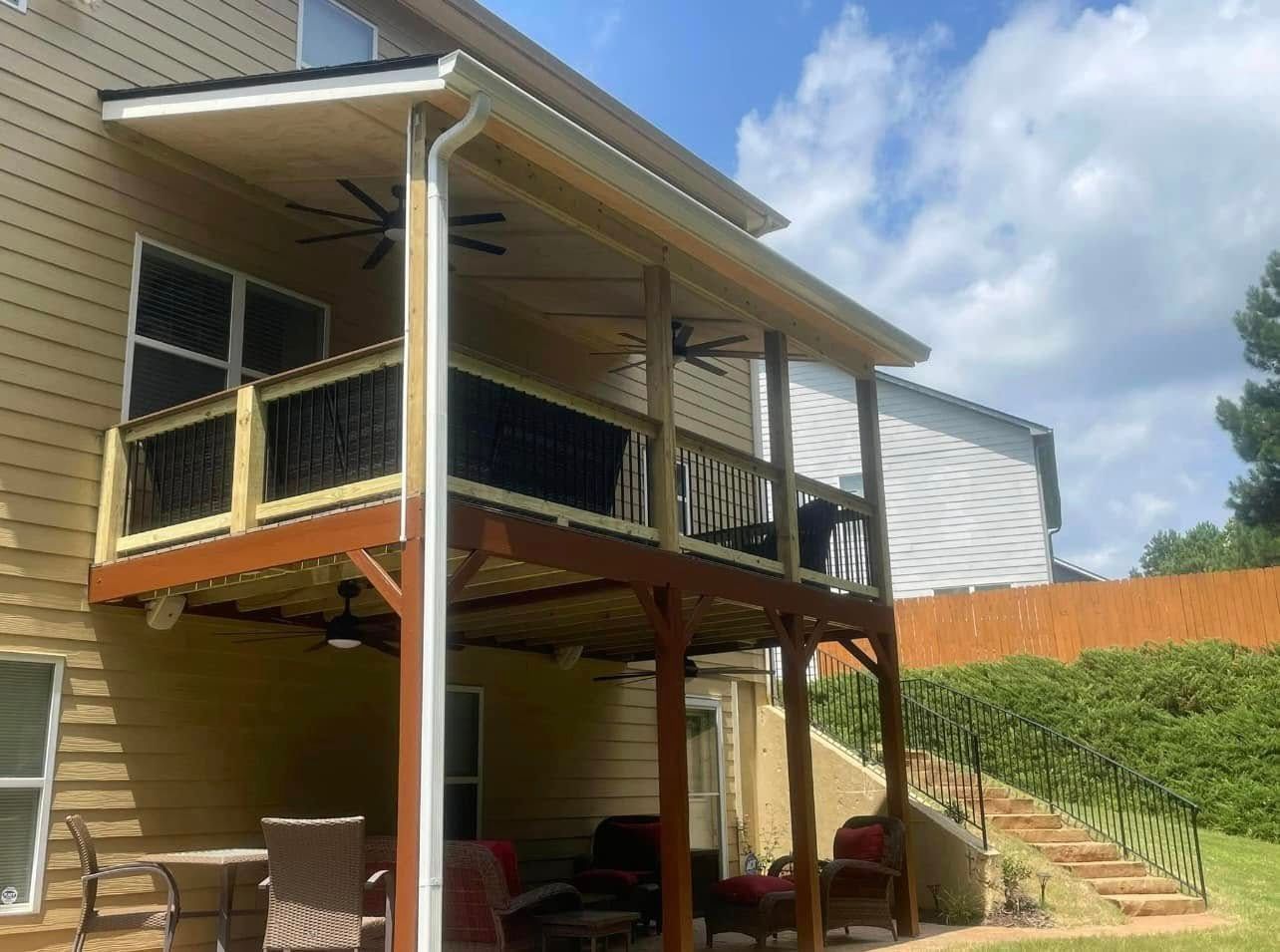 Raised wooden deck with railing and stairs on the back of a house, set against a grassy yard and blue sky
