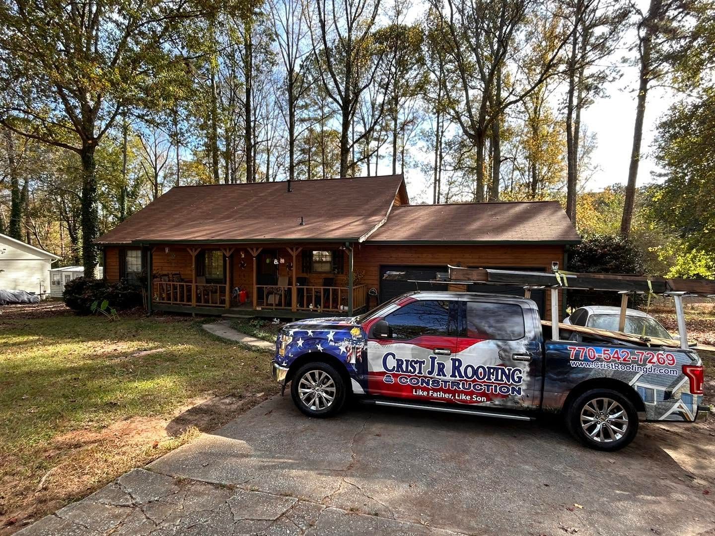 Truck with colorful promotional wrap parked in front of a rustic house and trees.