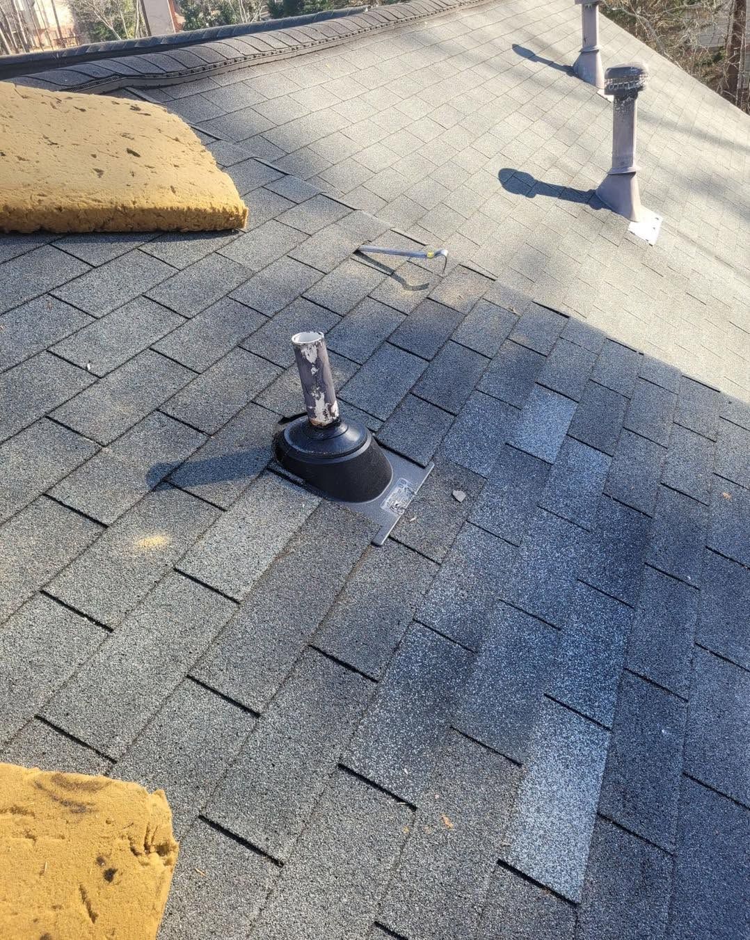 Rooftop shingles with two vent pipes and yellow foam blocks near the edges.