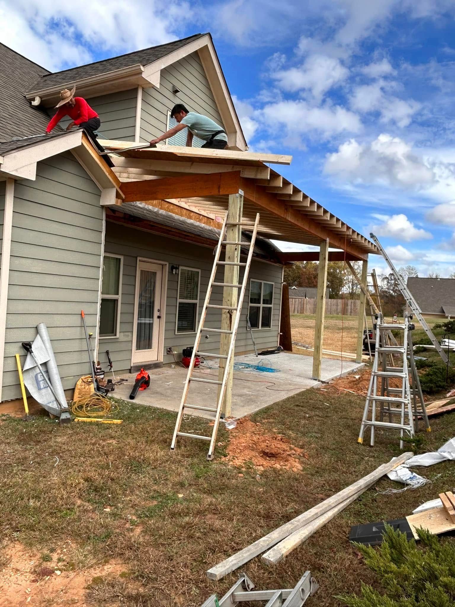 Workers installing a roof extension on a house with ladders and construction materials in the yard