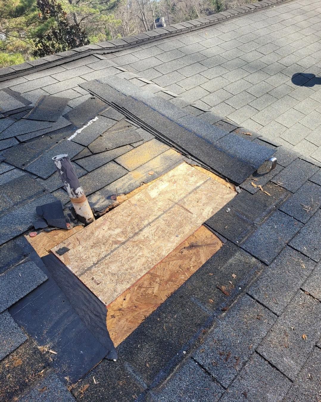 Damaged roof shingles with exposed plywood patch and vent pipe on a sloped roof