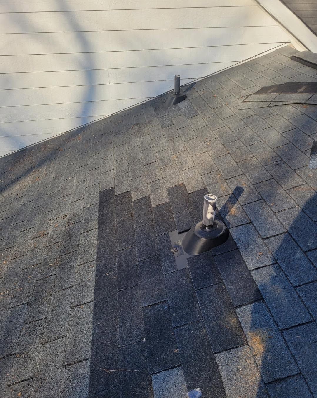 Gray shingled roof with two vent pipes and a small patch of missing shingles near the eave