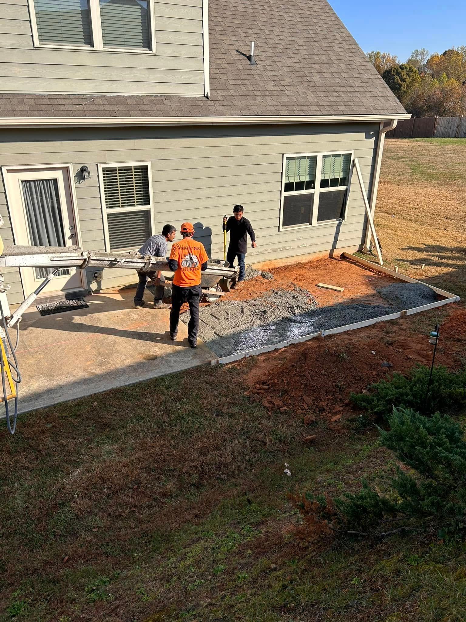 Workers in orange vests on a home patio, spreading gravel beside the house.