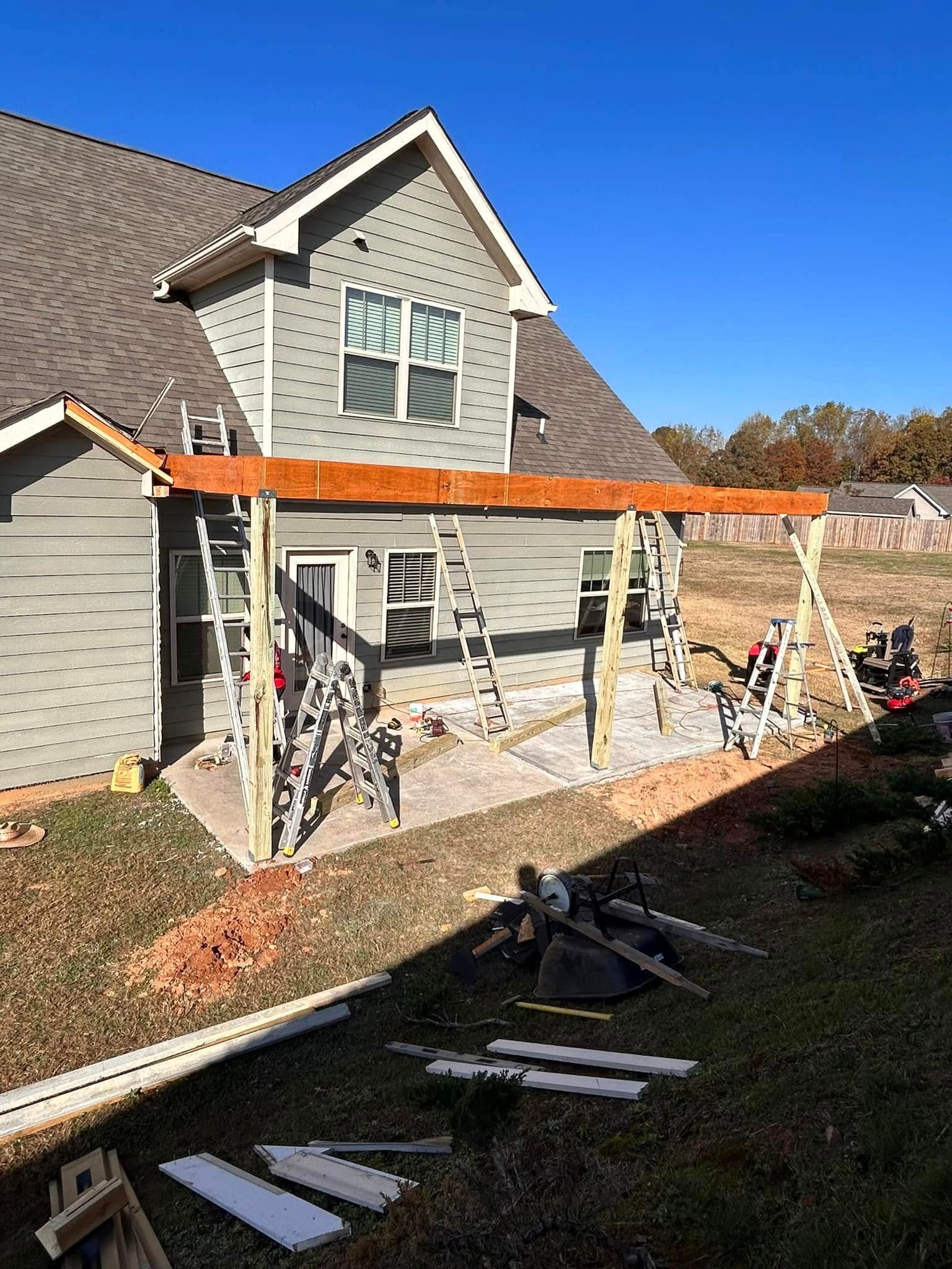 Home exterior with a wooden pergola under construction beside a gray house and stone patio