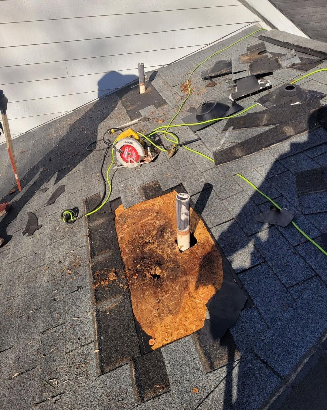 Rusted roof vent on asphalt shingles with scattered tools and a yellow extension cord during roof repair