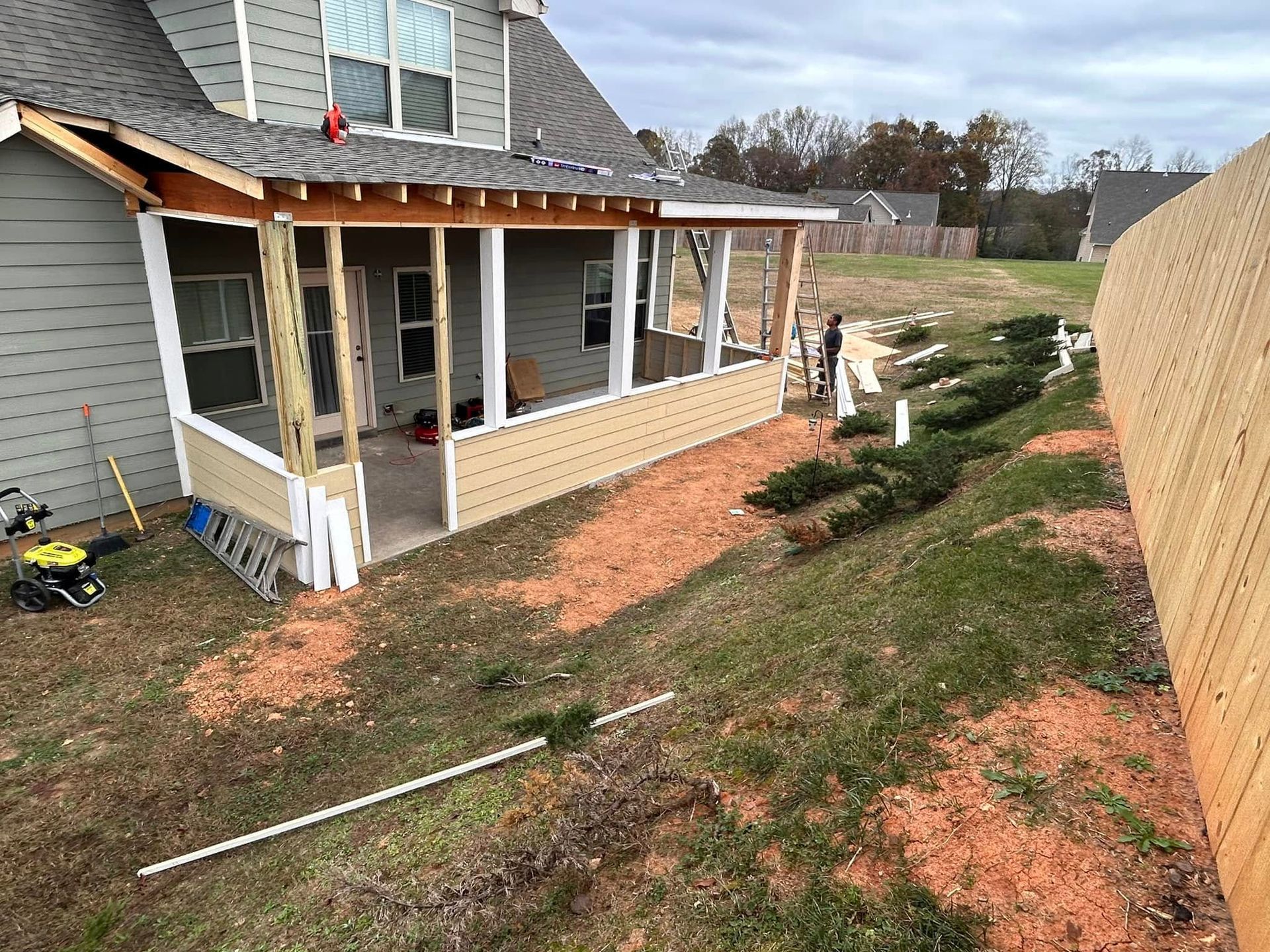House exterior under construction with exposed porch framing, brick base, and a dirt yard.