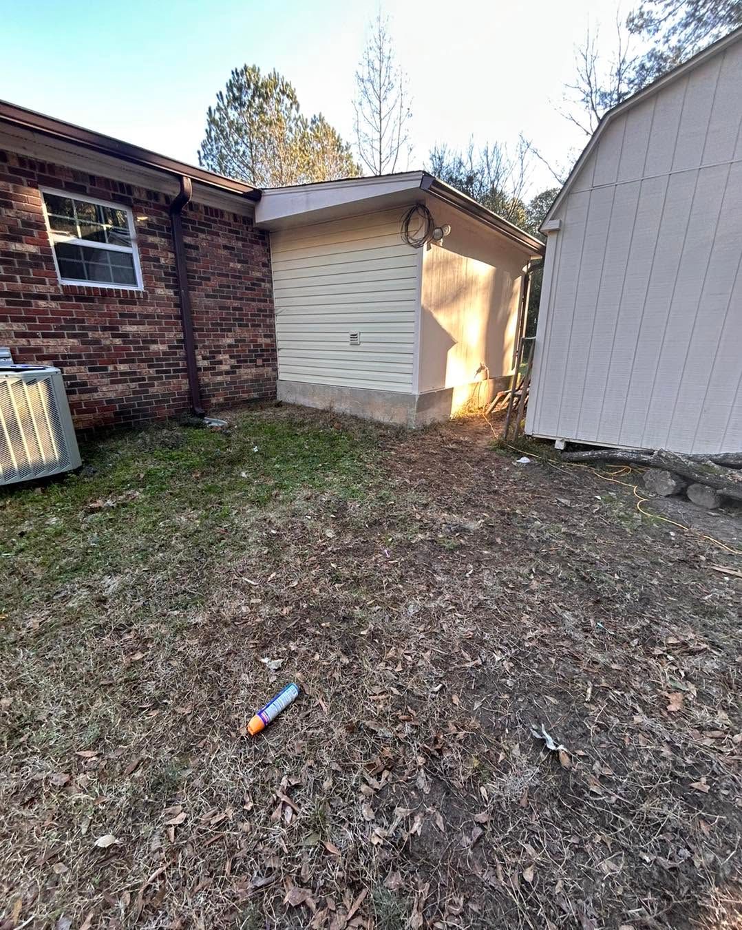 Backyard with brick and white sheds, leaf-covered ground, and a small orange bottle near the center