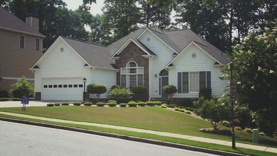 Suburban house with a manicured lawn, driveway, and trees along the street