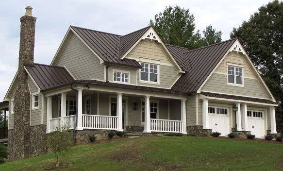 Large beige Victorian-style house with white trim, porch, and dark roof on a grassy hill
