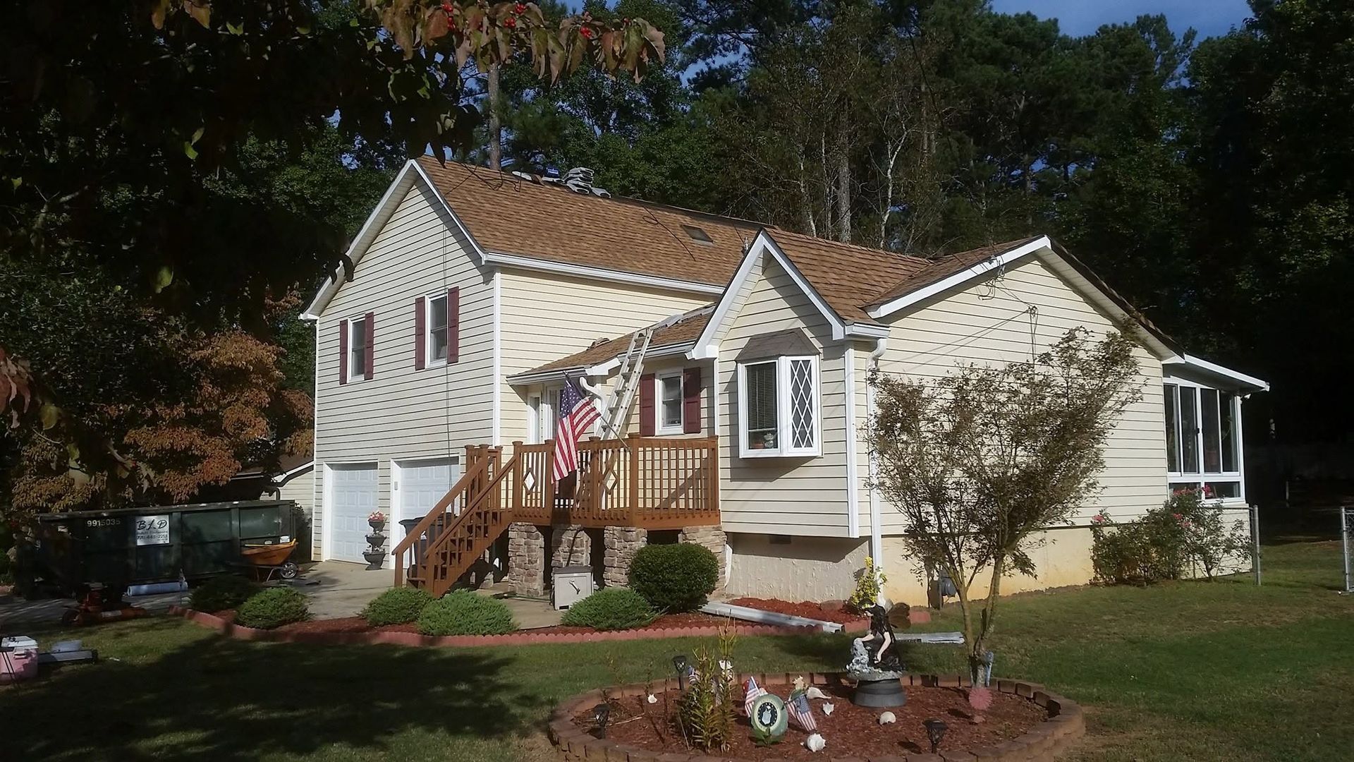 Suburban house with white siding, brown roof, front porch, and landscaped yard in daylight